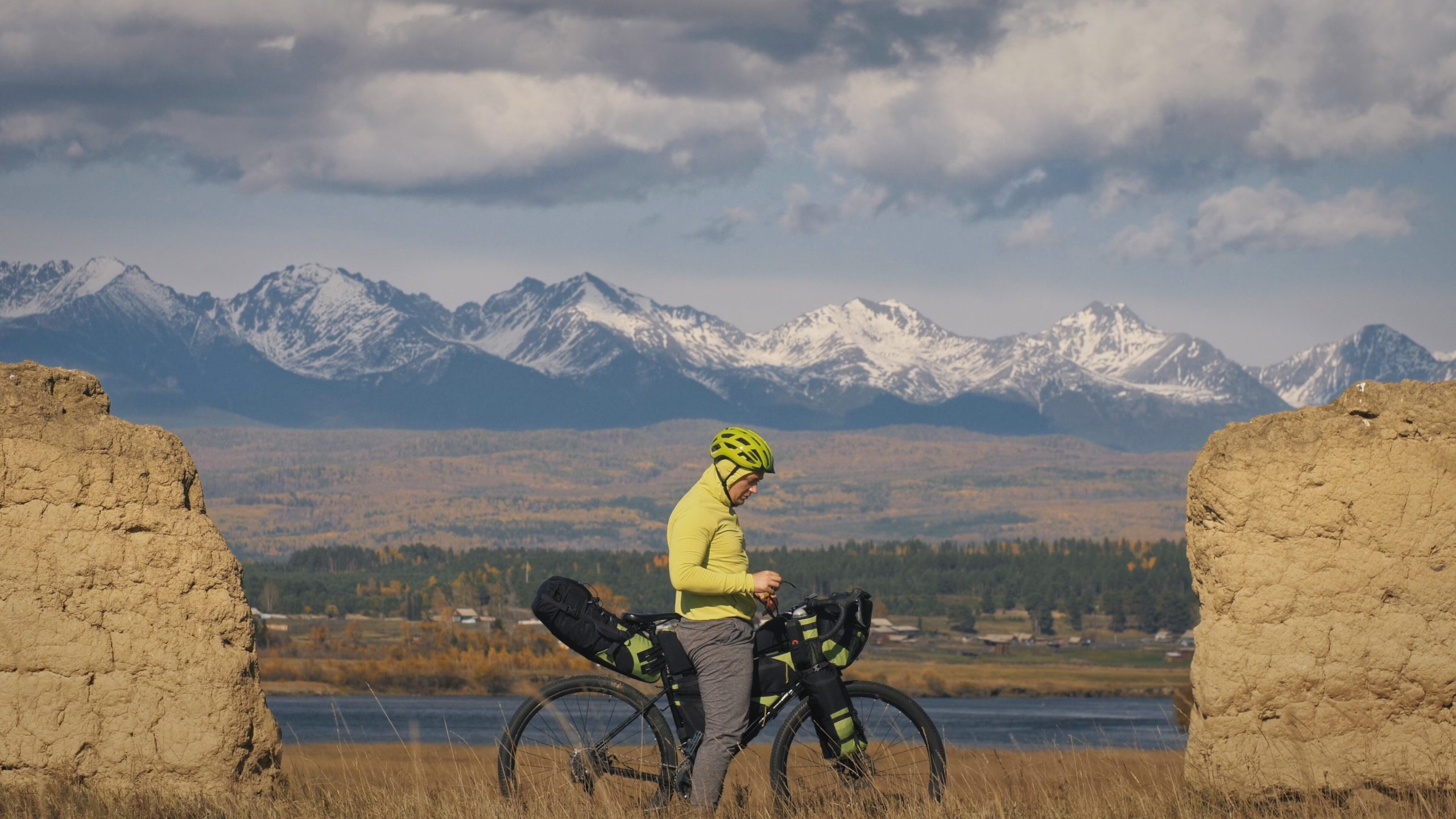 The man travel on mixed terrain cycle touring with bikepacking. The traveler journey with bicycle bags. Sport bikepacking, bike, sportswear in green black colors. Mountain snow capped, stone arch.