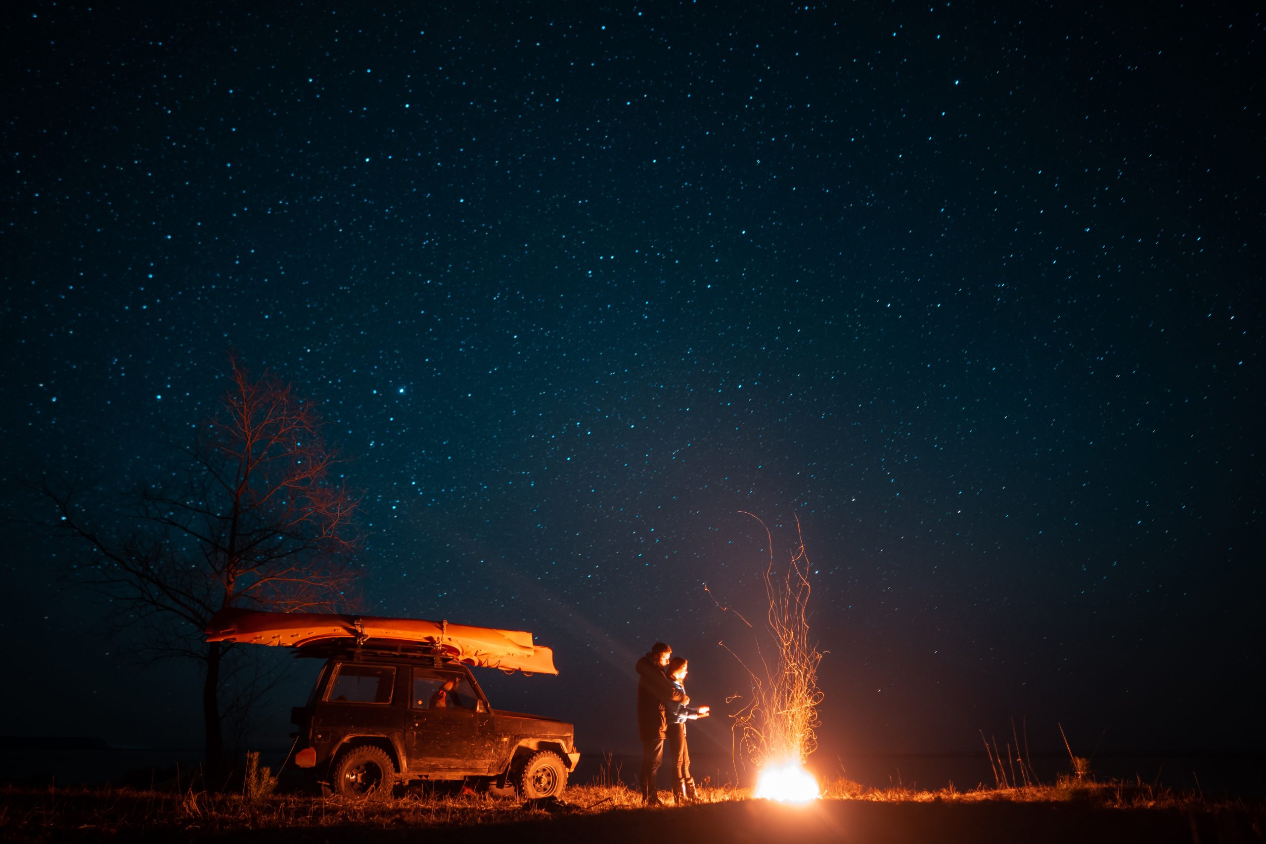 Happy couple man and woman standing in front burning bonfire under starry sky, enjoying quiet night